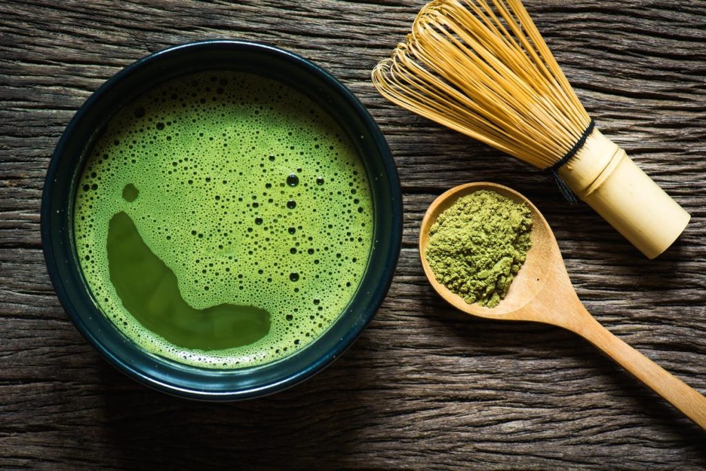Herbata matcha w kubku. Drewniana łyżka z proszkiem.